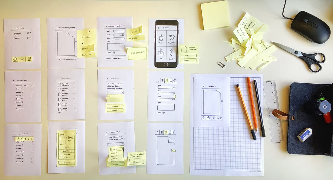 Paper wireframes, sticky notes and sketching tools laid out on a desk during early prototyping